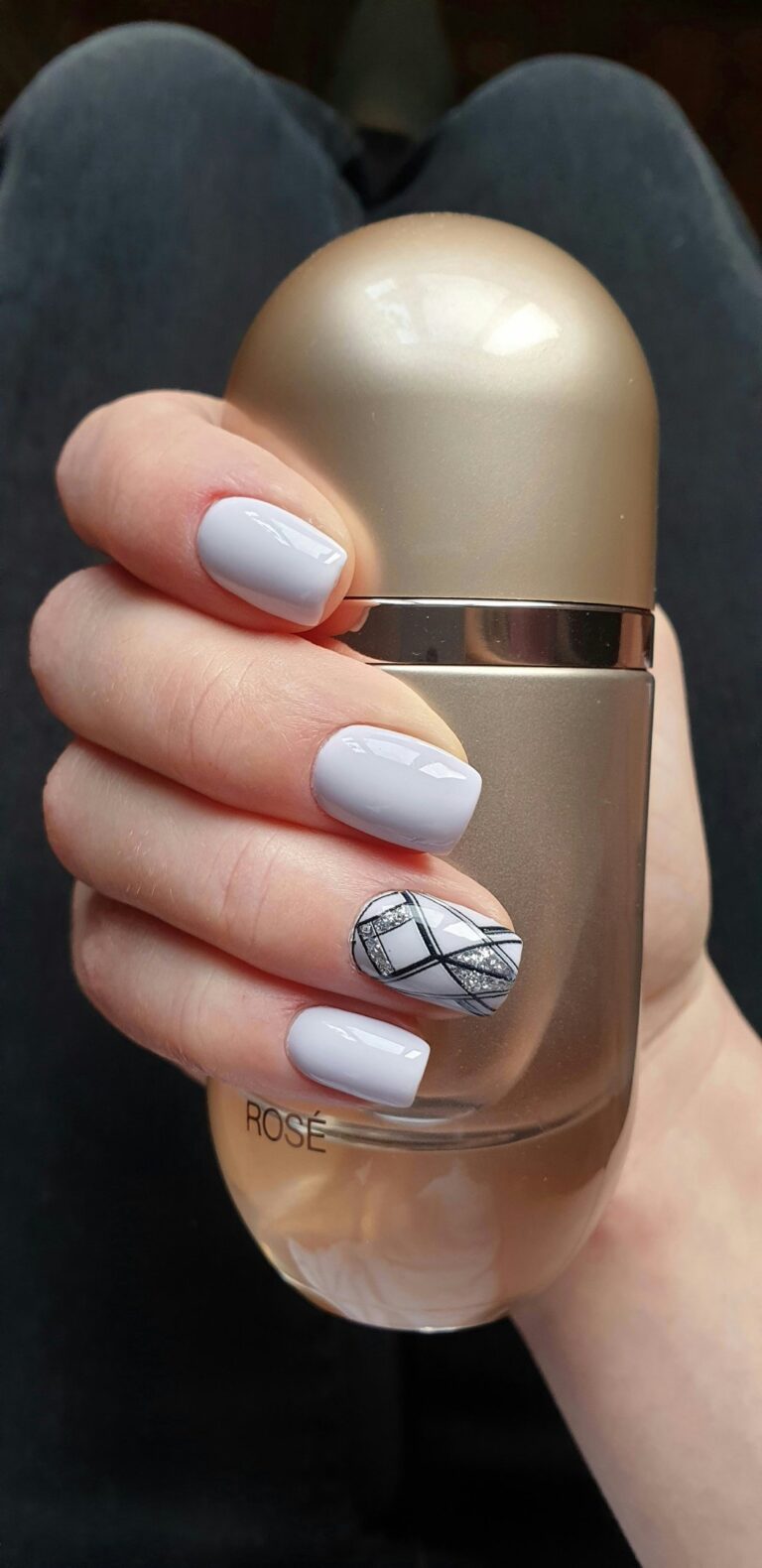 hands holding a bottle showing beautiful grey nails with a design